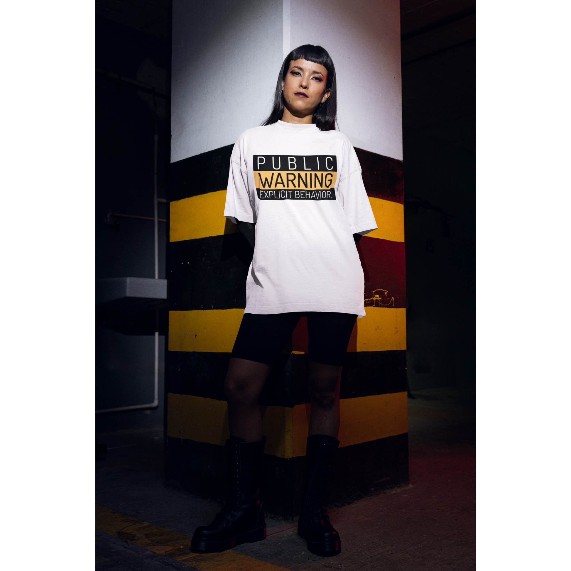 Hai người mặc áo thun trắng in chữ “PUBLIC WARNING: EXPLICIT BEHAVIOR” phong cách streetwear cá tính.