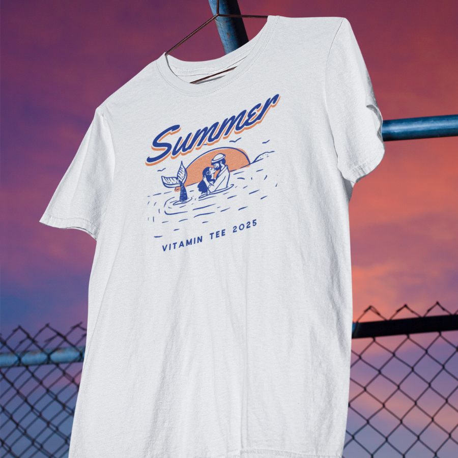 Áo thun trắng in hình nàng tiên cá và người lặn trong khung cảnh biển hoàng hôn, chữ “Summer – Vitamin Tee 2025”, màu cam và xanh biển phối tối giản.