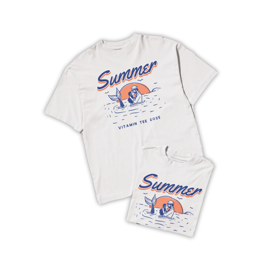 Áo thun trắng in hình nàng tiên cá và người lặn trong khung cảnh biển hoàng hôn, chữ “Summer – Vitamin Tee 2025”, màu cam và xanh biển phối tối giản.