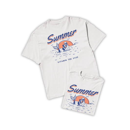 Áo thun trắng in hình nàng tiên cá và người lặn trong khung cảnh biển hoàng hôn, chữ “Summer – Vitamin Tee 2025”, màu cam và xanh biển phối tối giản.