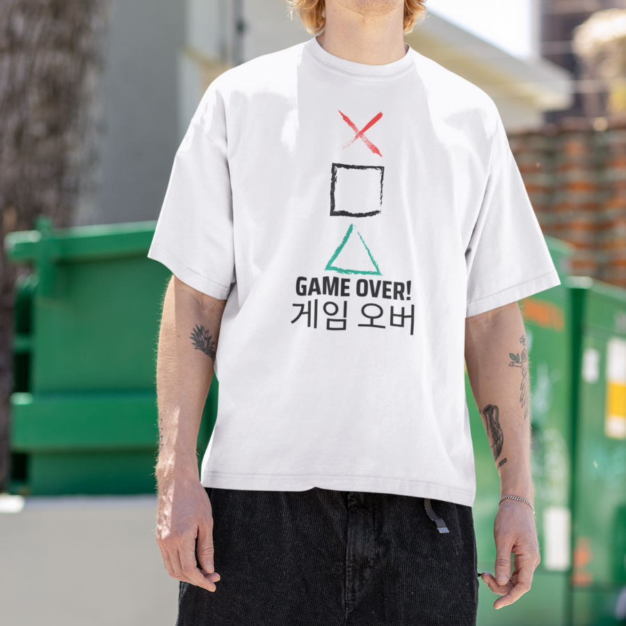 Áo thun trắng in hình biểu tượng Squid Game tam giác – vuông – dấu X đỏ, kèm dòng chữ “GAME OVER!” và tiếng Hàn