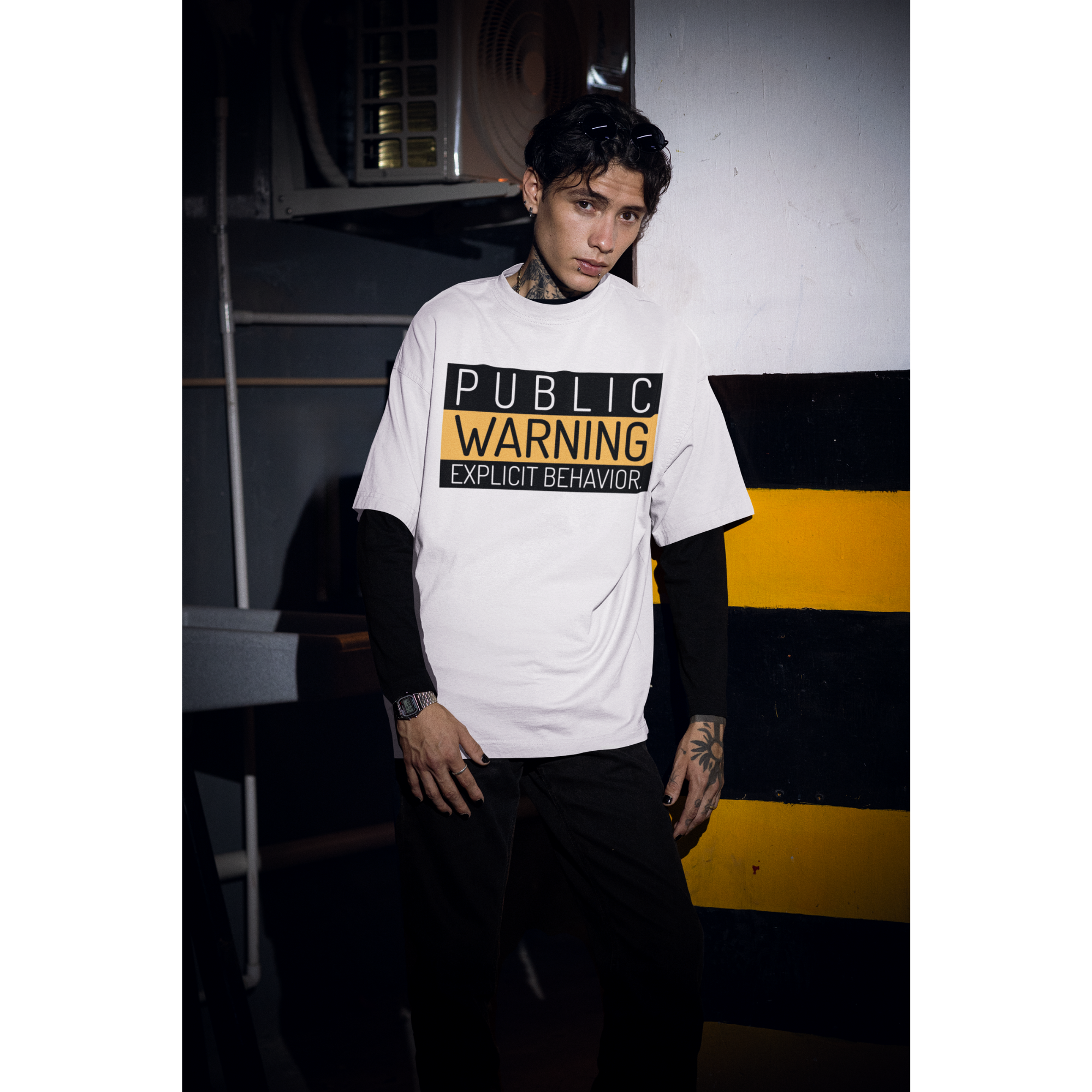 Hai người mặc áo thun trắng in chữ “PUBLIC WARNING: EXPLICIT BEHAVIOR” phong cách streetwear cá tính.