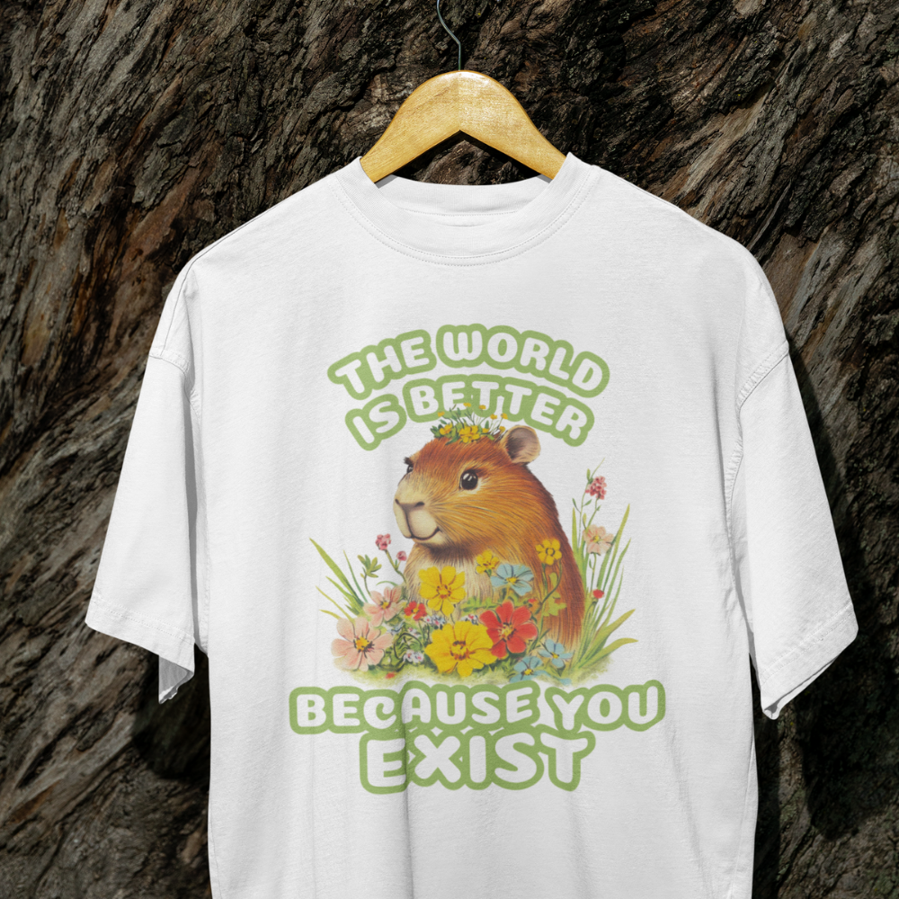 White t-shirt with a graphic of a guinea pig and flowers, text 'The world is better because you exist', on a wooden hanger against a textured brown background.